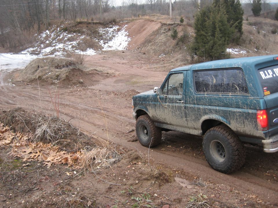 1996 Ford Bronco driving off-road, covered in mud. Rear window has 'R.I.P. D.' sticker