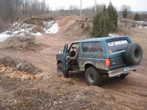1996 Ford Bronco - A green Ford Bronco navigates a muddy off-road course with a driver visible inside.