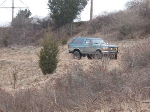 1996 Ford Bronco - A green Ford Bronco is parked on a hillside with dry brush and a few trees.