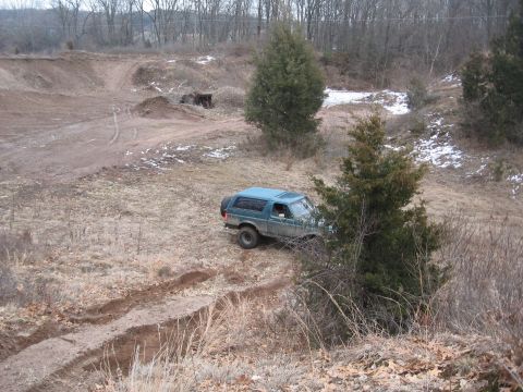 1996 Ford Bronco - Blue 1996 Ford Bronco navigates a challenging dirt path in a wooded, winter landscape.