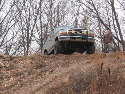 1996 Ford Bronco - A person stands on a hill next to a lifted Ford F-Series truck, which is angled on the incline.