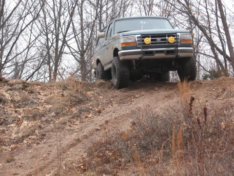 1996 Ford Bronco - A green Ford Bronco navigates an off-road trail on a cloudy day.