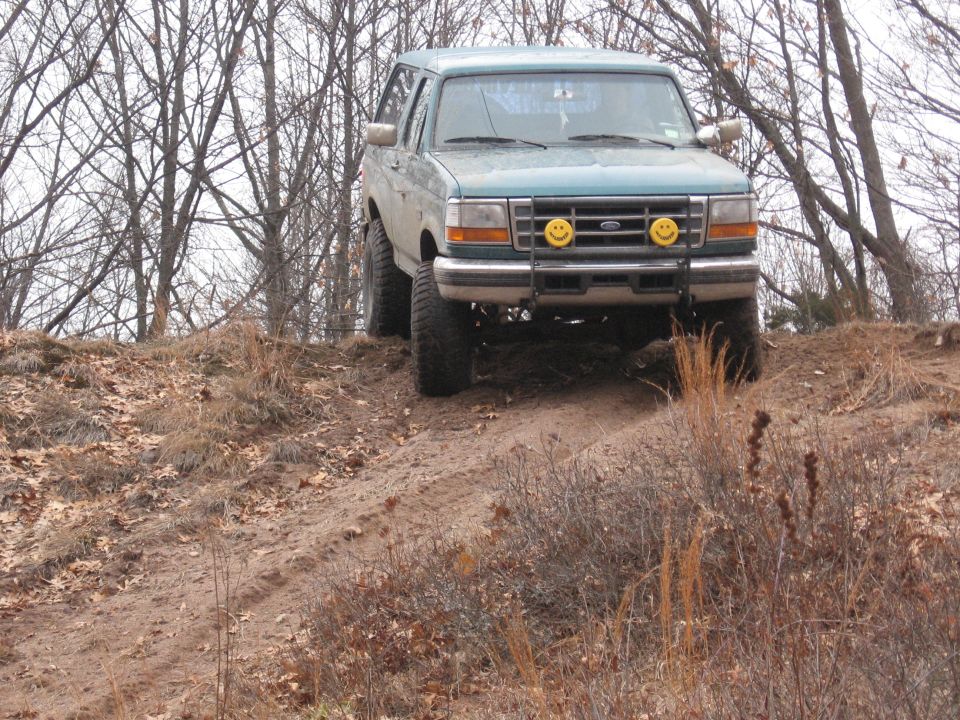 Teal 1996 Ford Bronco with smiley face headlights driving on a dirt hill