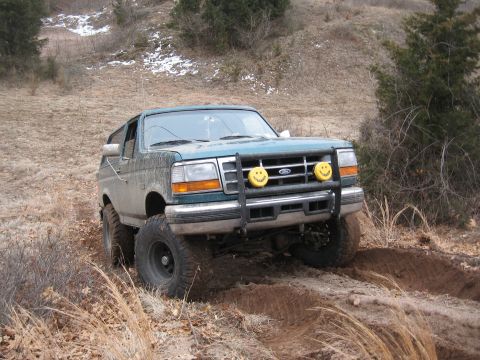 1996 Ford Bronco - A green 1996 Ford Bronco navigates a dirt track with a bull bar and smiley face fog lights.