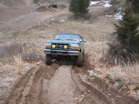 1996 Ford Bronco - A 1996 Ford Bronco navigates a muddy, off-road trail with visible tire tracks in the dirt.