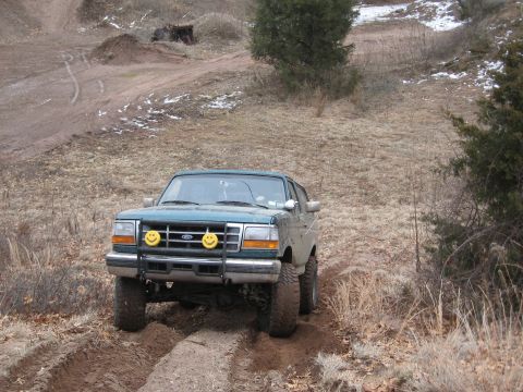 1996 Ford Bronco - A green Ford Bronco navigates a muddy trail in a dry, grassy landscape.