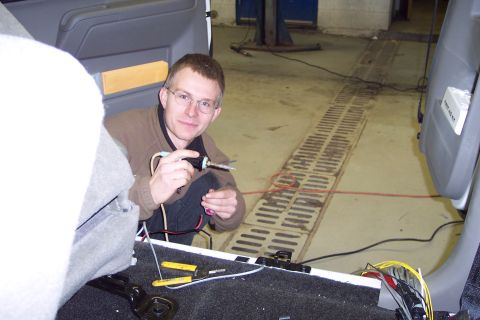 2001 Ford Crown Victoria - A man works on wiring inside the rear of a vehicle, with tools and electrical components visible.