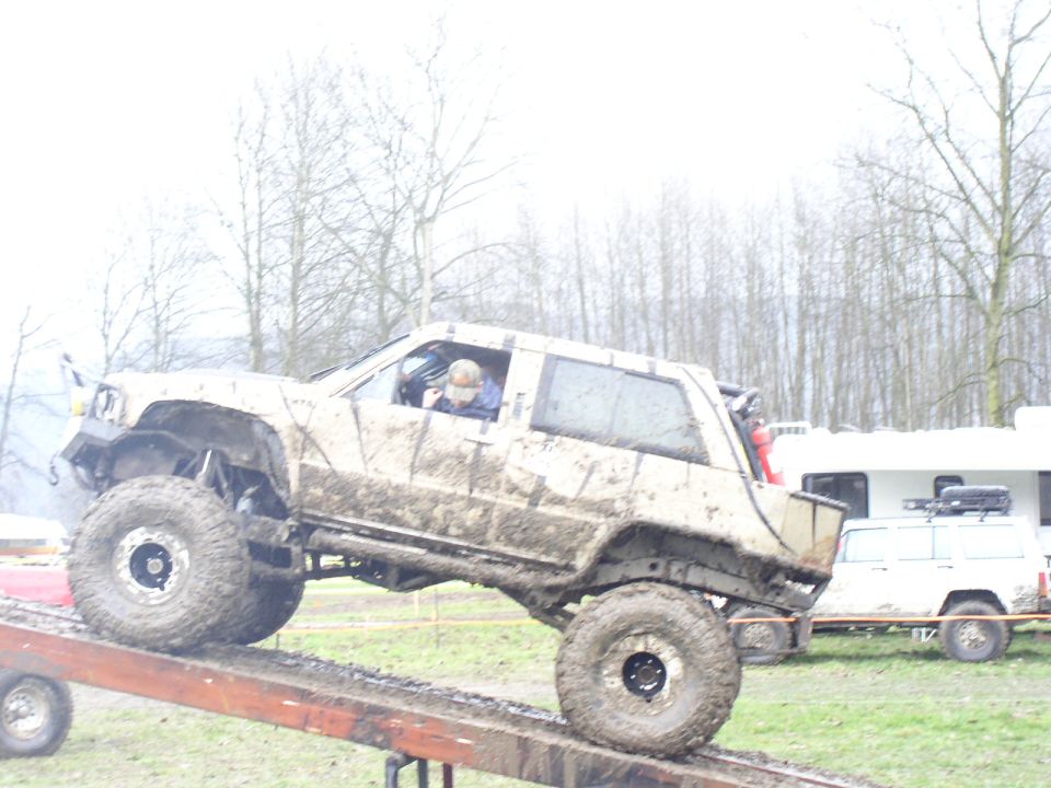 muddy off-road SUV on ramp, another SUV and trailer in background
