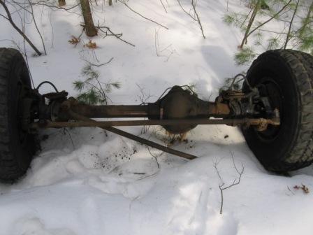 1993 Ford Bronco - A vehicle's rear axle and tires are partially buried in snow amidst a wooded area.