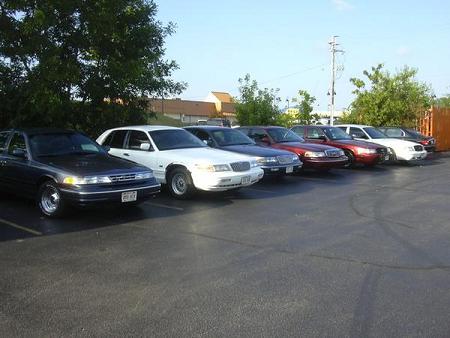 1997 Mercury Grand Marquis - A row of cars are parked in a lot under a clear sky.