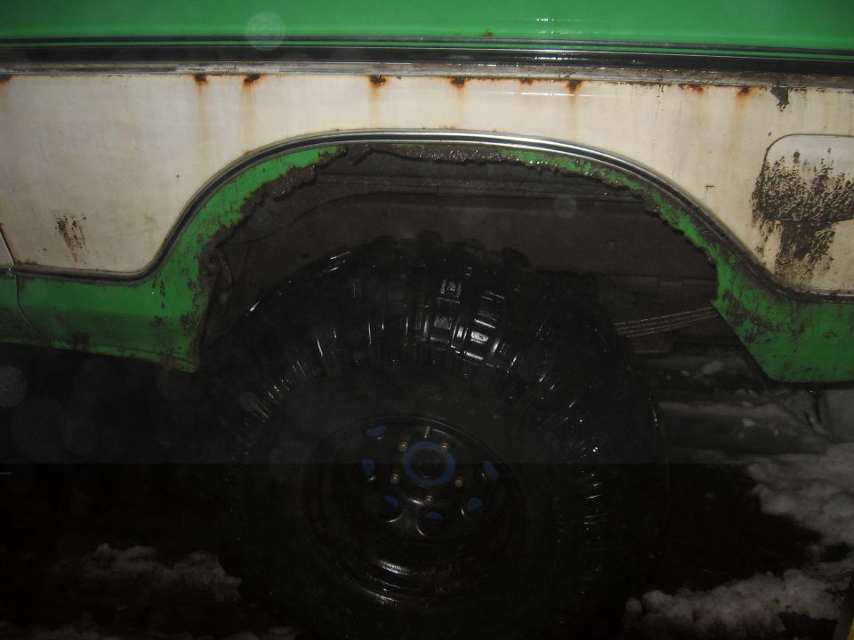 Green and white vehicle's rusty rear wheel well and large tire