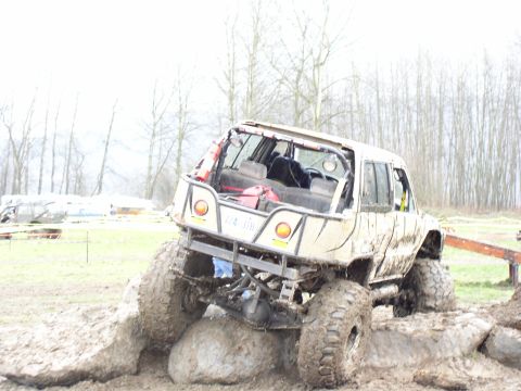 Modified off-road SUV with large tires stuck on rocks in mud. Roll cage visible
