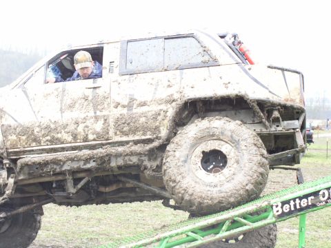 Mud-covered off-road vehicle with large tires on a ramp, driver visible inside