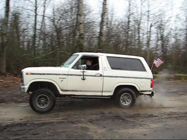 White 1980 Ford Bronco driving through mud with an American flag on the back