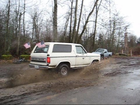 1980 Ford Bronco - White 1980 Ford Bronco driving through a muddy area with American flags on the back.
