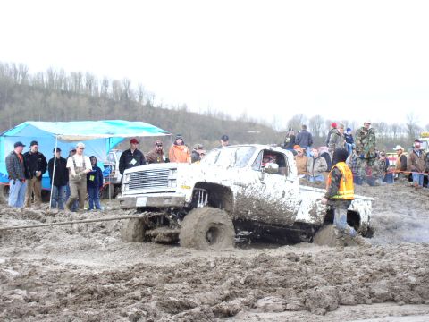 Mud-covered pickup truck stuck in deep mud, with spectators watching
