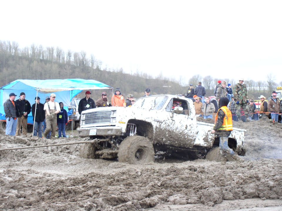 Mud-covered pickup truck stuck in deep mud, with spectators watching