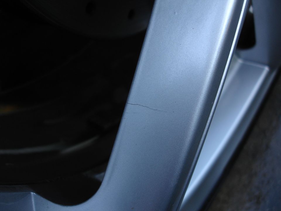 Close-up of a silver alloy wheel rim with a visible crack on one of the spokes