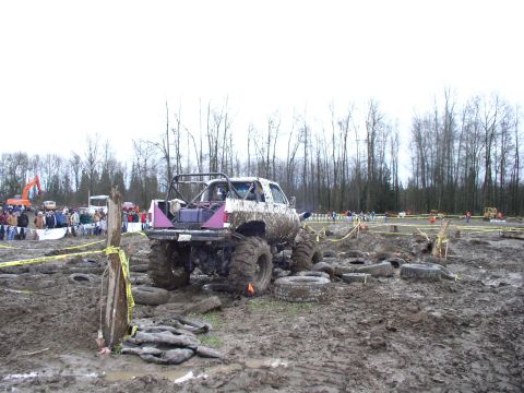 Muddy lifted truck with roll cage in a mud pit with tires scattered around