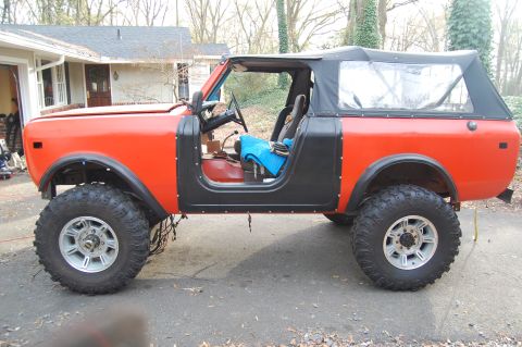 1994 Ford Bronco - An orange International Harvester Scout II is parked in a driveway, showing its lifted suspension and off-road tires.