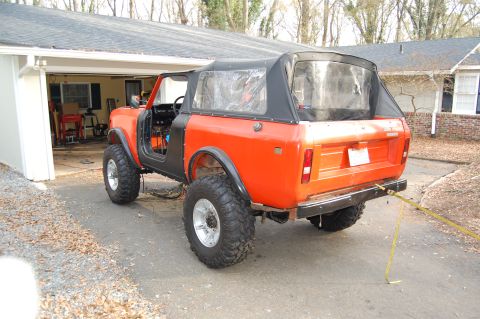 1994 Ford Bronco - This orange SUV features a black soft top and is modified with a lifted suspension and large off-road tires.