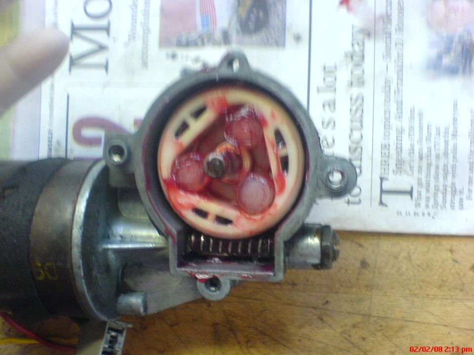 Window regulator mechanism with red grease and gears, resting on newspaper