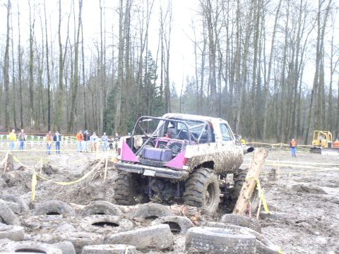 Mud-covered off-road vehicle with roll cage and large tires, viewed from the rear