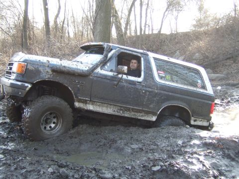 1976 Toyota Land Cruiser - Ford Bronco deep in mud, stuck off-road. Driver is visible in the cabin.