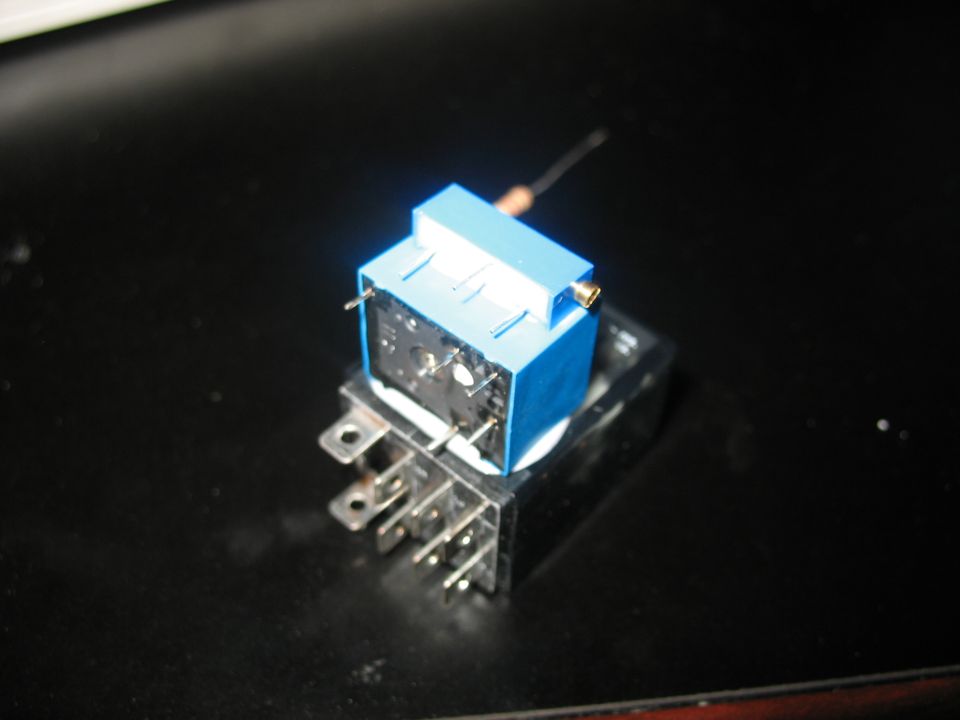 Blue and black electrical relay with metal pins on a dark surface