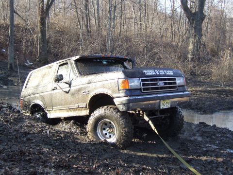 1976 Toyota Land Cruiser - A mud-covered Ford Bronco is stuck in a muddy ditch, with trees in the background.
