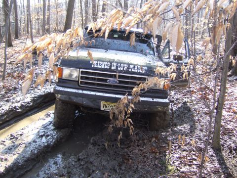 1976 Toyota Land Cruiser - Ford F-Series truck navigating a muddy trail in a wooded area.