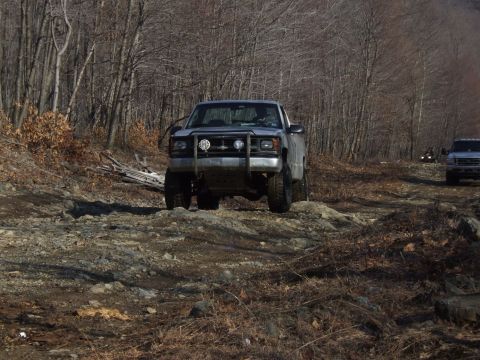 1976 Toyota Land Cruiser - A silver pickup truck navigates a challenging rocky trail, with another vehicle visible in the distance.