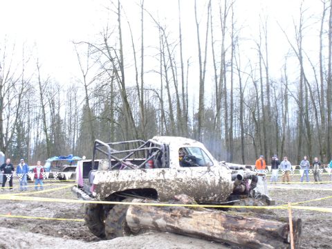 Muddy pickup truck with roll cage in a race, people watching in background