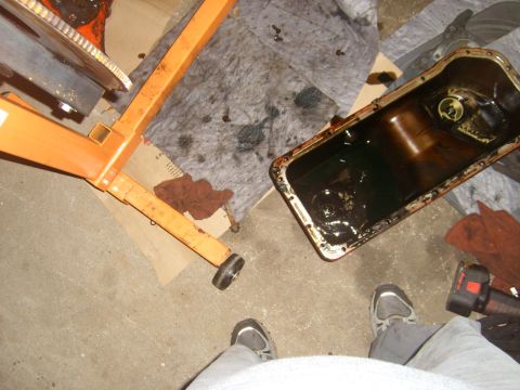 1994 Ford Bronco - An engine oil pan, removed from a vehicle, sits on a garage floor next to an engine hoist.