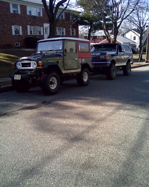 1989 Ford Bronco - Two off-road vehicles, a classic Toyota Land Cruiser and a Ford Bronco, are parked side-by-side on a residential street.