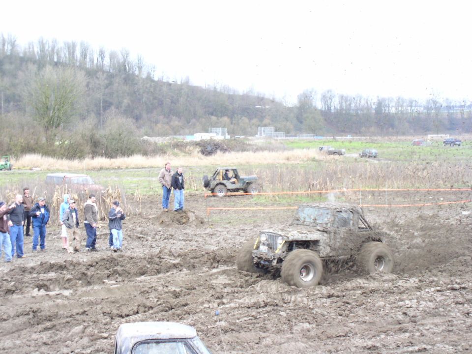 Off-road vehicles stuck in mud during a competition. People watch from the side