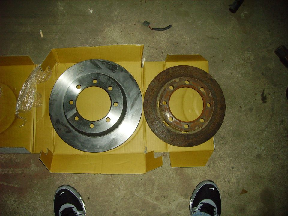 New machined 8-lug brake rotor beside the rusty original on yellow boxes
