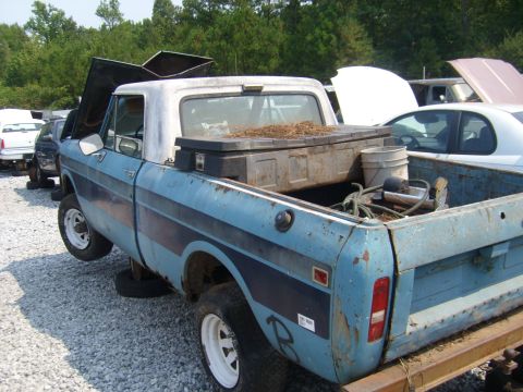 1994 Ford Bronco - A blue pickup truck sits in a junkyard with its hood open and a toolbox in the bed.
