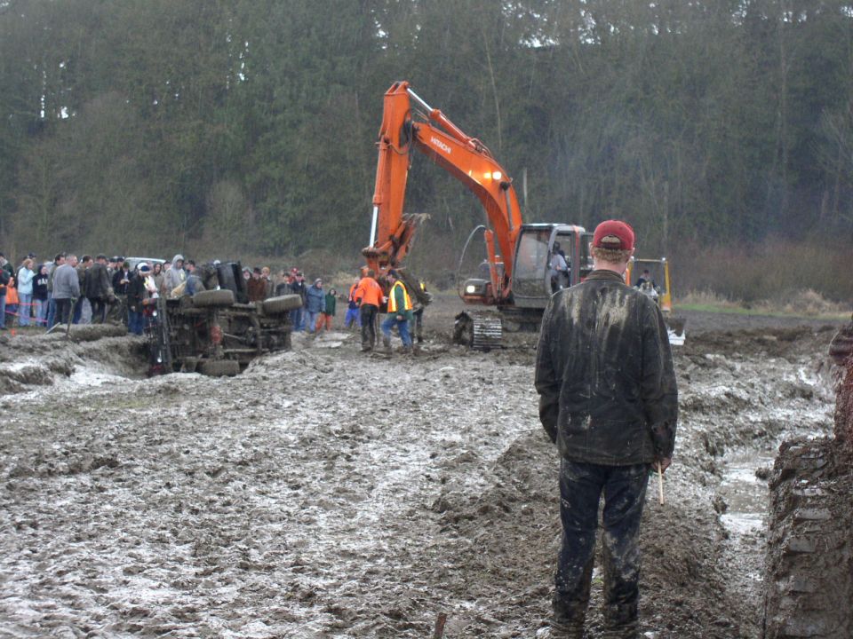 Overturned vehicle in mud pit with excavator and crowd