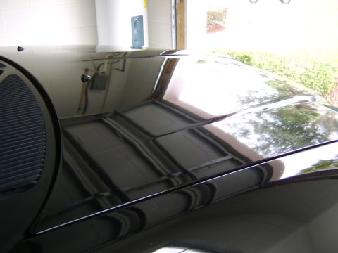 1996 Mercury Grand Marquis - The glossy hood of a black vehicle reflects the surroundings, including a water heater and garage door.