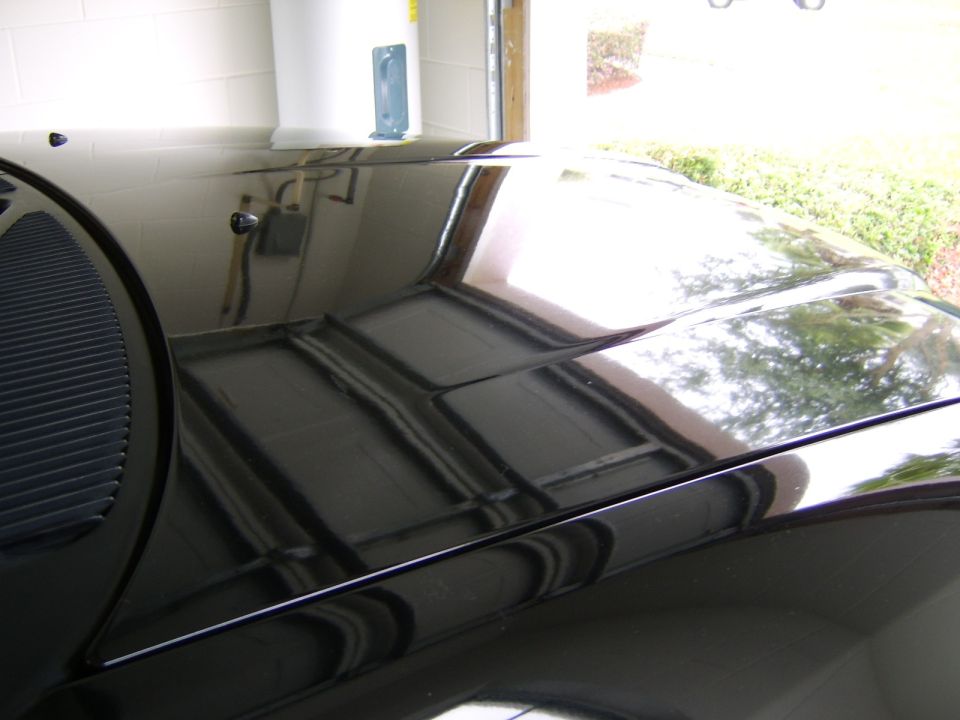 Glossy black car hood reflecting garage rafters and open door after polishing