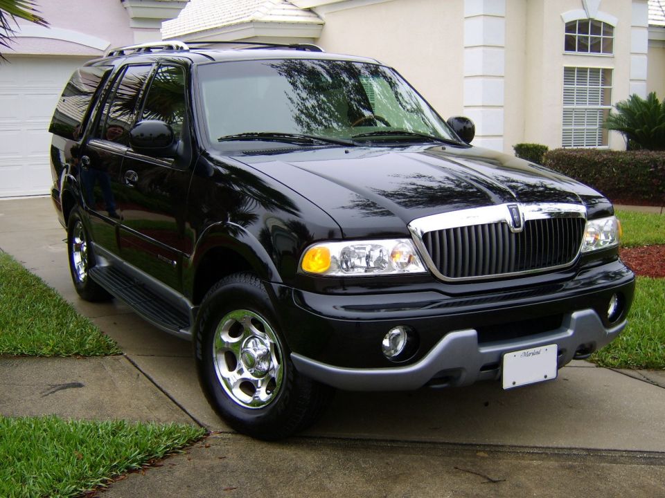 Black Lincoln Navigator SUV, front 3/4 view on a driveway beside a stucco house