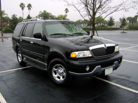 1996 Mercury Grand Marquis - This black SUV, likely a 1998 Lincoln Navigator, is parked in a wet, empty lot.