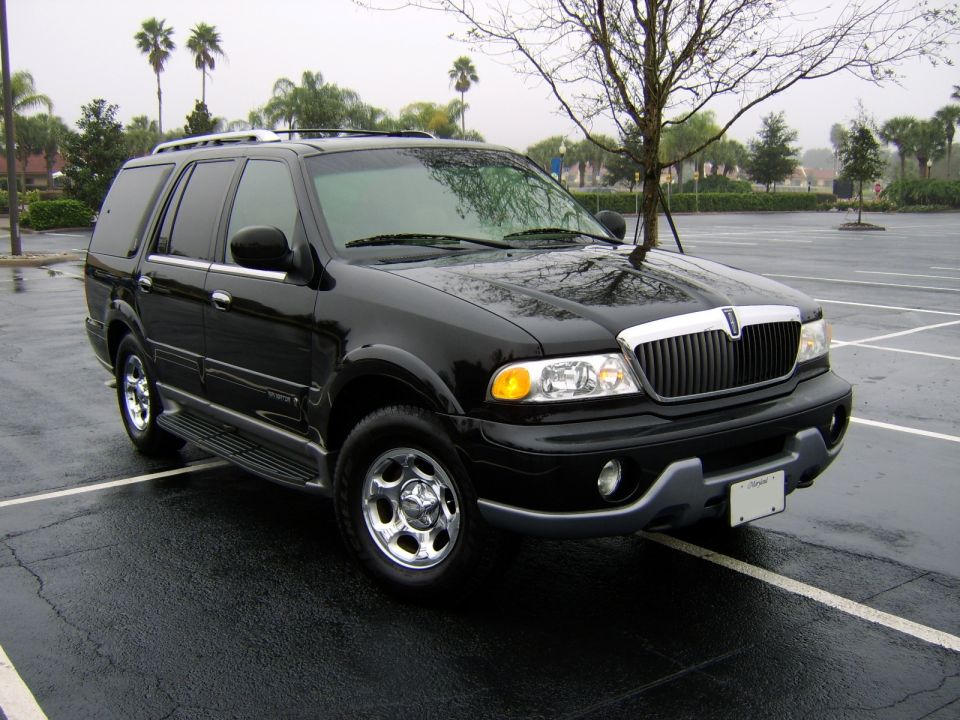 Black Lincoln Navigator SUV parked on a wet lot with palm trees behind