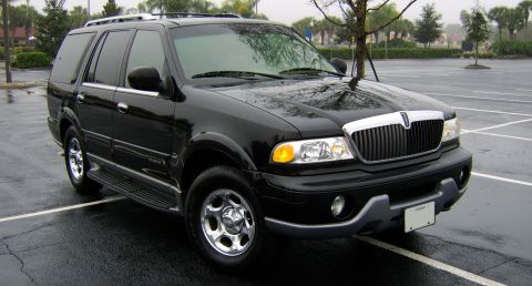 1996 Mercury Grand Marquis - A black Lincoln Navigator is parked in a wet parking lot under a cloudy sky.