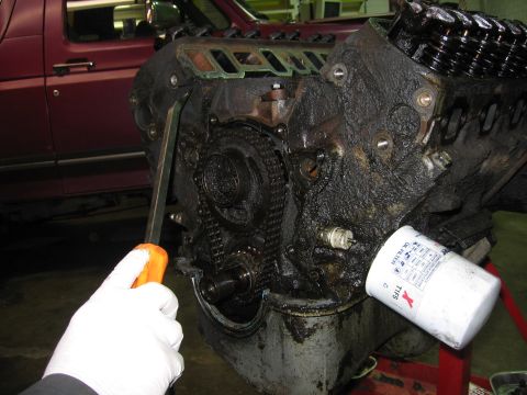1990 Ford Bronco - A mechanic works on a greasy engine, with a maroon vehicle visible in the background.
