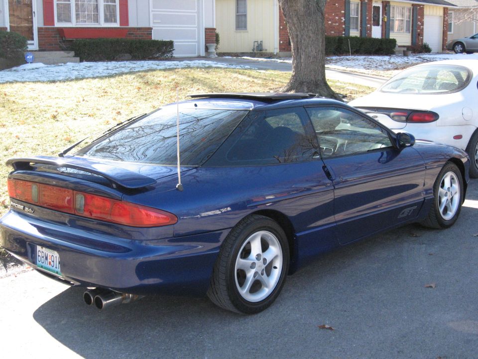 Blue 1995 Ford Probe GT coupe with a rear spoiler, dual exhaust, and a sunroof, parked on a residential street