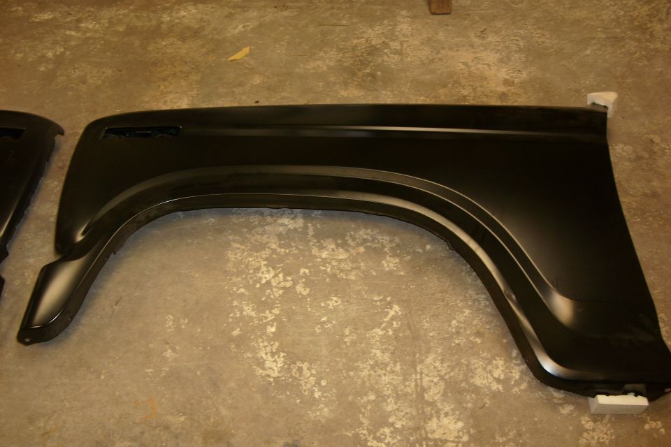 Black painted front fender panels lying on a concrete shop floor