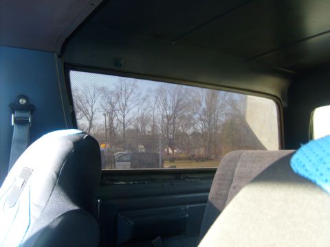 1989 Ford Bronco - View from inside a vehicle's passenger seat, looking out the side window at a rural landscape with trees and buildings.