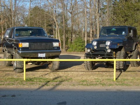 1989 Ford Bronco - Two lifted off-road vehicles, a Ford Bronco and a Jeep CJ, are parked outdoors.